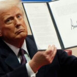 Donald Trump holding up a signed executive order document at a press briefing.