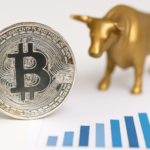 Close-up of a physical Bitcoin coin with a blurred bull figurine and rising bar graph in the background, symbolizing bullish sentiment and Bitcoin-DeFi growth.
