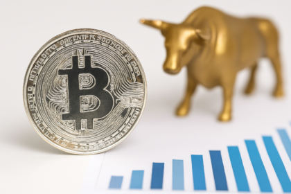 Close-up of a physical Bitcoin coin with a blurred bull figurine and rising bar graph in the background, symbolizing bullish sentiment and Bitcoin-DeFi growth.